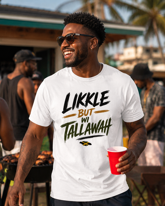 A man wearing a white graphic t-shirt with the text 'LIKKE BUT WI TALLAWAH' in black and green, holding a red cup at an outdoor barbecue.